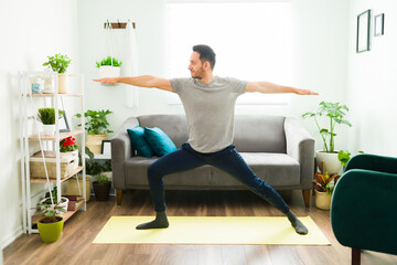 Hispanic man practicing a warrior 2 yoga pose at home