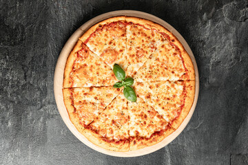 Hot tasty traditional italian pizza with salami, meat, cheese, tomatoes greens on a dark background