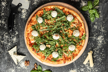 Hot tasty traditional italian pizza with salami, meat, cheese, tomatoes greens on a dark background