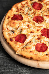 Hot tasty traditional italian pizza with salami, meat, cheese, tomatoes greens on a dark background