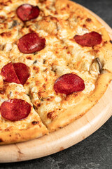 Hot tasty traditional italian pizza with salami, meat, cheese, tomatoes greens on a dark background