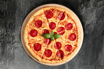 Hot tasty traditional italian pizza with salami, meat, cheese, tomatoes greens on a dark background
