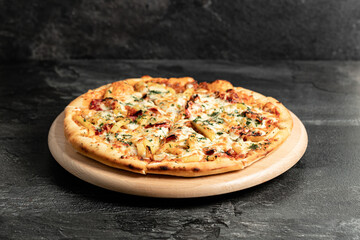 Hot tasty traditional italian pizza with salami, meat, cheese, tomatoes greens on a dark background