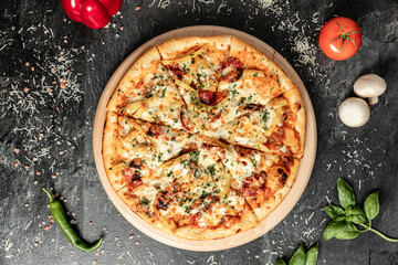 Hot tasty traditional italian pizza with salami, meat, cheese, tomatoes greens on a dark background