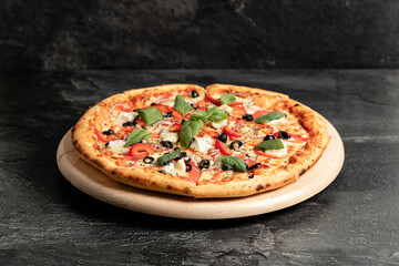 Hot tasty traditional italian pizza with salami, meat, cheese, tomatoes greens on a dark background