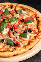 Hot tasty traditional italian pizza with salami, meat, cheese, tomatoes greens on a dark background