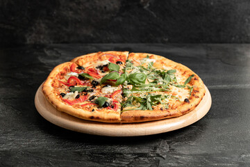 Hot tasty traditional italian pizza with salami, meat, cheese, tomatoes greens on a dark background