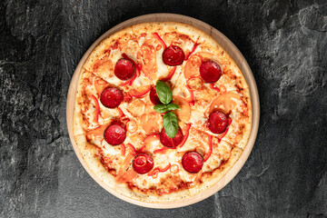 Hot tasty traditional italian pizza with salami, meat, cheese, tomatoes greens on a dark background
