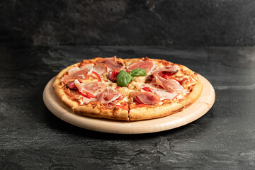 Hot tasty traditional italian pizza with salami, meat, cheese, tomatoes greens on a dark background