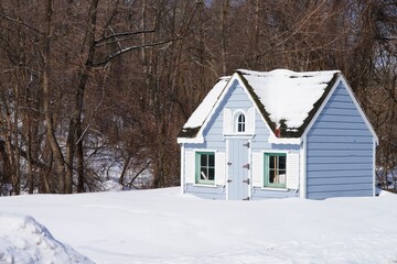 Winter view of a cute tiny house garden shed with white shutters after a snowfall