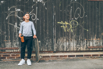 Teenager skateboarder boy standing beside a wooden grunge graffiti wall with skateboard and Water bottle flask. Youth generation Freetime spending and active people concept image. - Powered by Adobe