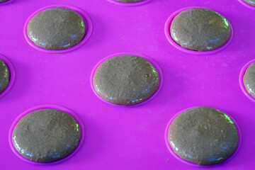 Homemade chocolate raspberry macaron cookies on a pink silicone mat on a baking sheet
