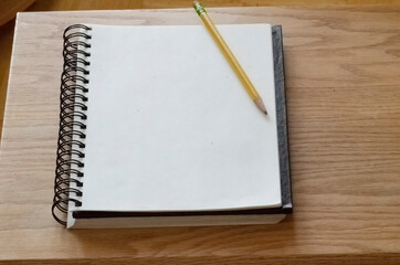 Angled sketch pad and pencil on top of pad on wooden table
