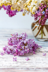 Purple lilac in glass vase on white wooden table. Spring branches of blooming lilac festive bouquet of flowers. Purple lilac branch on table, floral still life on gray wooden background.