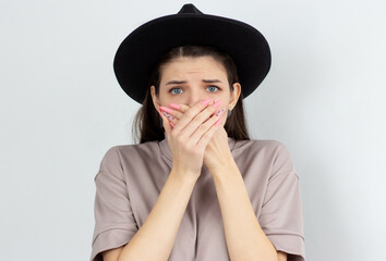 Scared woman covering her mouth with hands over white background and looking at camera