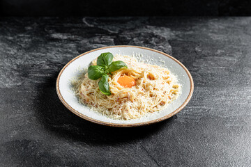 Pasta Carbonara on white plate with parmesan and yolk on dark marble background