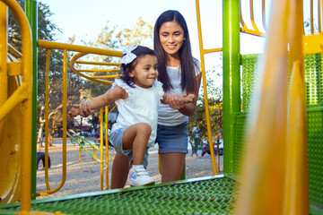 Niña sube a un juego en parque para niños con ayuda de su mama