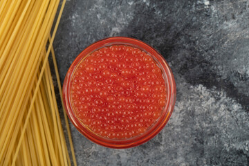 A glass plate of red sturgeon caviar with uncooked pasta