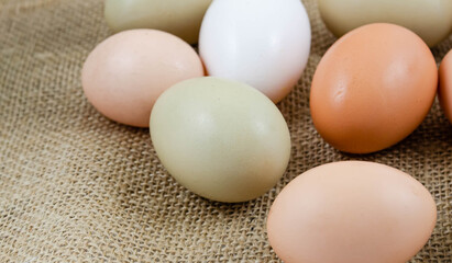 A collection of backyard chicken eggs in different colors on burlap fabric
