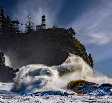 Huge wave crashing on headland under Cape Disappointment lighthouse near mouth of Columbia River, Ilwaco, WA. Lighthouse and center of wave are sharp, exterior of wave is blurred to emphasize motion