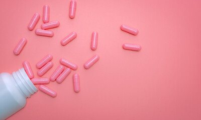 Pink capsule spread out of white plastic drug bottle. Capsule and pill bottle on pink background. Vitamins and supplements for healthy skin, collagen boost, and acne treatment concept. Online pharmacy