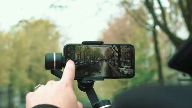 A man that starts to film the Amsterdam canals on his phone with a gimbal.