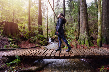 Girl Walking on a Mystical Trail in Rain Forest during a foggy and rainy Winter Season. Woods in Squamish, North of Vancouver, British Columbia, Canada. Low Angle Panorama