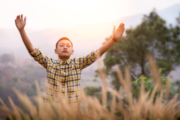 Boy arms raised to pray and worship God in the meadow in the evening sunset. Young Christian concept.