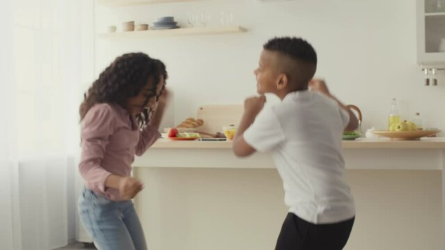 Happy black little brother and sister dancing together at kitchen, having fun and home