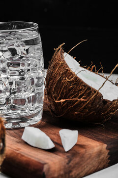 Half cut coconut on wooden board and glass of water with ice