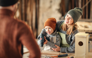 Mother and kid using drill in carpentry workshop