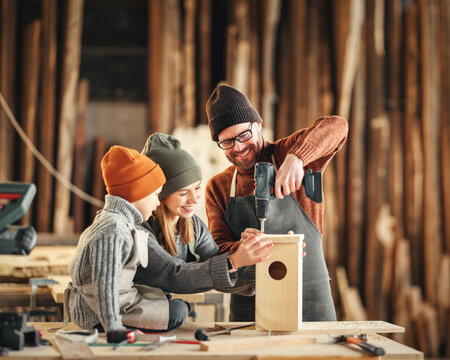 Kid with parents assembling wooden bird house in craft workshop