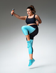Sporty girl jumping with dumbbells. Photo of model with curvy figure in fashionable sportswear on...
