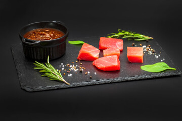 Fresh tuna fillet steaks with spices, sauce and herbs on a black background. Preparing tuna for baking