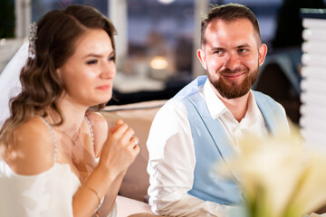 newlyweds sit at table in restaurant and listen to congratulations from guests.