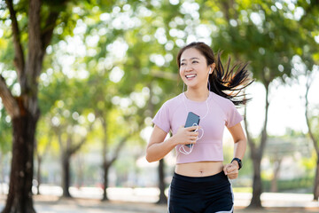 Healthy Asian woman running in the morning in the park. She smiled joyfully while jogging.