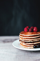 Juicy pancakes with berries and honey on a white plate, spoon, wooden table