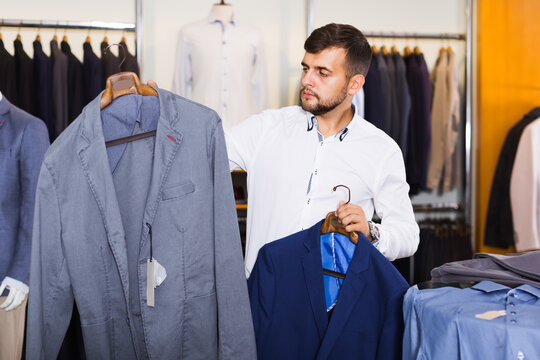 Cheerful man customer choosing jacket in men clothes shop
