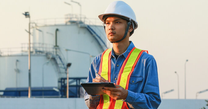asian engineering working inside oil and gas refinery plant ,checking quality using digital tablet on a storage tank background