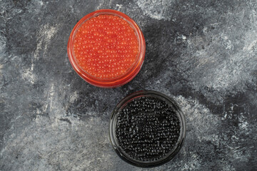 Glass plates full of red and black caviar on a marble background