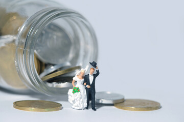 Wedding budget concept miniature people, toys photography. Bride and groom with coin money on a jar glass isolated on white background. Image photo