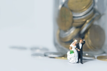 Wedding budget concept miniature people, toys photography. Bride and groom with coin money on a jar glass isolated on white background. Image photo