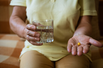 Mature woman with a glass of water holds a tablet in her hand while sitting on the couch. Treatment concept