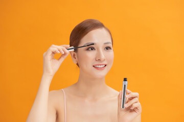 Obraz premium young beautiful woman Applying mascara isolated on yellow