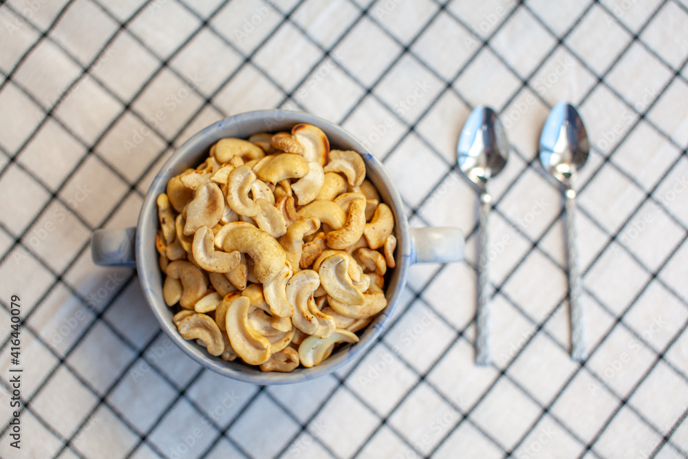 Poster a plate of cashew nuts on a nice napkin and two spoons next to it.