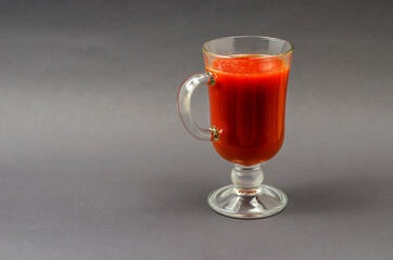 A full goblet of tomato juice on a gray background.