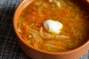 Cabbage soup with sour cream in a brown earthen bowl on a blue tablecloth.