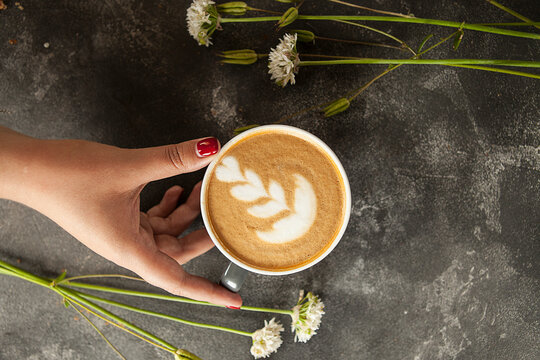 female hand holds a cup of aromatic cappuccino or latte, top view