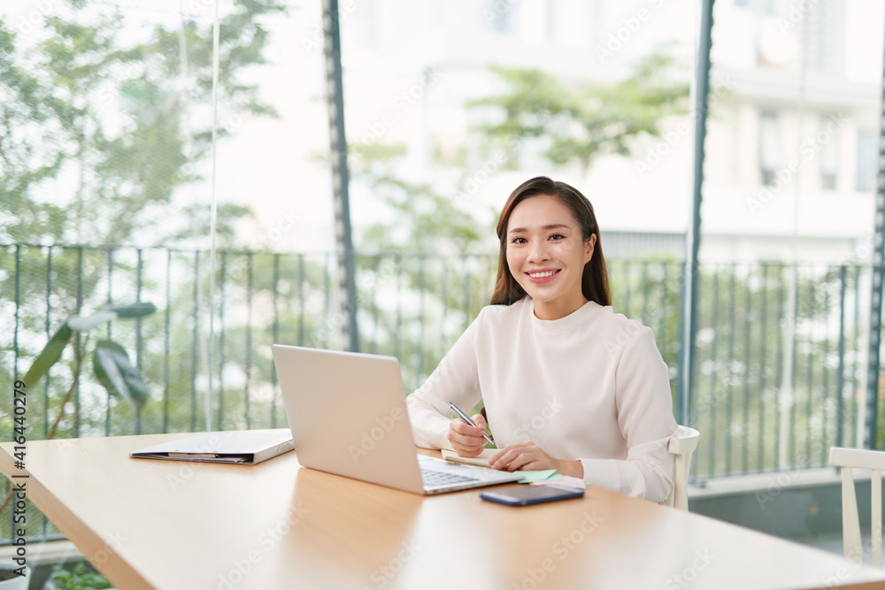 Poster single happy female business owner with smile on phone and working on laptop computer at desk with b