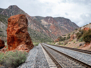 Tall vertical red boulder beside railroad tracks.